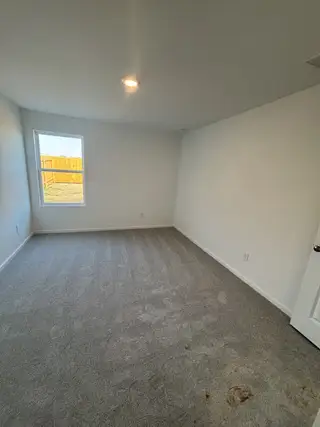 A cozy room with fresh carpet, white walls, and a window that lets in natural light, creating an inviting atmosphere.