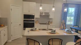 A modern kitchen with sleek white cabinets, an island, elegant pendant lighting, and stylish decor.