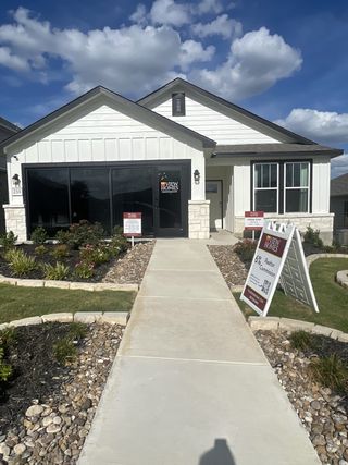 A charming model home with white siding and stone accents, showcasing View Homes at The Meadows at Hunters Ranch (San Antonio, TX), with realtor information displayed. 