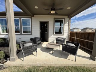 A covered patio with four gray woven chairs, a wicker table, a ceiling fan, and a view of a fenced backyard with a cloudy sky.