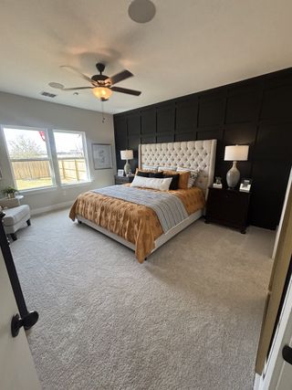 A luxurious and spacious master suite with a black paneled accent wall, a tufted beige headboard, and stylish decor.