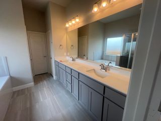 A sleek bathroom featuring a double vanity, large mirror, elegant lighting, and a shower with natural light enhancement.