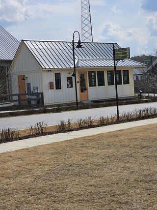 Model Home A charming building with light siding and a metal roof features a peach-colored door and signage for City Hall, Police, and Court, located in Harmony by Kinglett Homes (Auburn, GA).