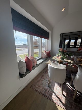A cozy dining nook with a cushioned window seat, elegant chairs, and a rustic table, bathed in natural light.