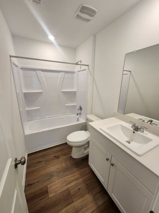 A modern bathroom featuring a sleek white tub, single sink vanity, and wood-style flooring.