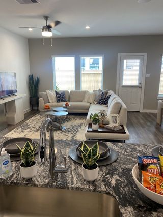 A cozy living room with a neutral sectional, modern decor, and a granite kitchen counter with plants and snacks.