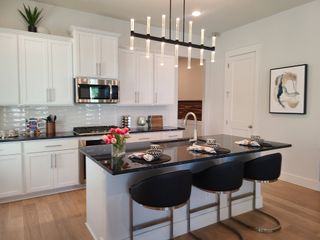 A modern kitchen with sleek white cabinets, a black countertop island, stylish lighting, and wooden floors.