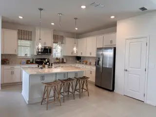 A modern kitchen with sleek white cabinetry, light pendant lights, and a spacious island with bar seating