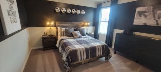 A modern bedroom featuring a wooden bed, plaid bedding, and soccer-themed decor. Warm lighting and dark accents enhance the cozy feel.