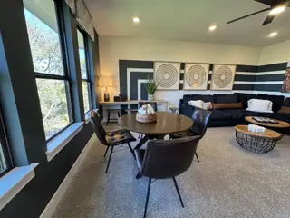 A spacious living area with modern decor, featuring cozy seating, a round table, and large windows with natural views.