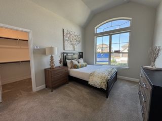 A cozy bedroom with a large window, elegant bed, wooden furniture, and an adjacent walk-in closet.