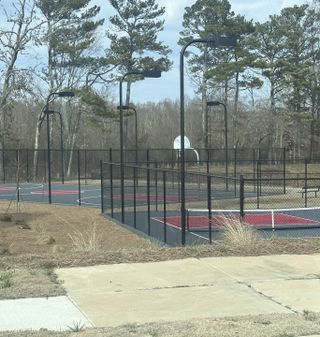 Outdoor sports area with basketball and pickleball courts, surrounded by a fence and trees in Dacula, GA.