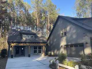 A charming gray home nestled among trees with a spacious driveway in Carolina Bay by Center Park Homes (Ridgeville, SC).