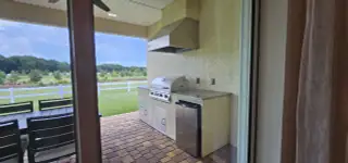 An inviting outdoor kitchen with a sleek built-in grill, mini fridge, and charming patio overlooking lush green landscape.