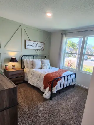 A cozy bedroom with soft carpeting, a decorative accent wall, and natural light in Copes Landing by D.R. Horton (Jacksonville, FL).