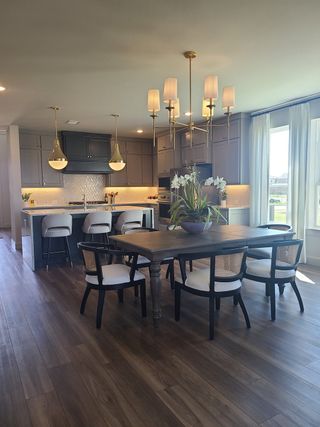 A modern kitchen features sleek cabinetry, a chic dining area, pendant lighting, and hardwood floors.