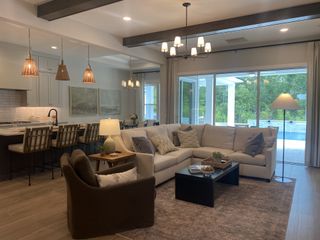 A cozy living room with a sectional sofa, elegant lighting, and large windows overlooking a lush garden and pool.