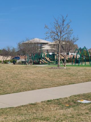 Street view A vibrant playground with shade structures in Star Trail - 65s by American Legend Homes, Prosper, TX, surrounded by greenery.