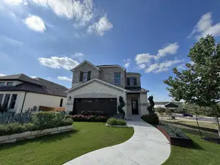 Street view A charming two-story stone and brick home with a well-manicured lawn and winding pathway in Sweetwater by Pulte Homes (San Antonio, TX).