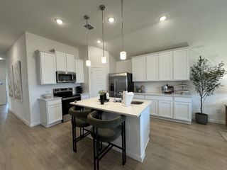 Model Home A modern kitchen featuring white cabinetry, a central island with seating, and sleek appliances. Bright and open with stylish lighting.