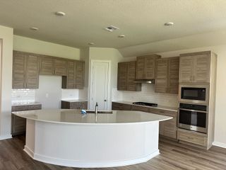 A modern kitchen featuring woodgrain cabinets, a curved island, and sleek stainless steel appliances.