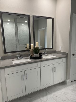 A sleek bathroom featuring a dual-sink vanity, elegant mirrors, and bright marble tiles for a modern touch.