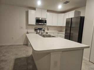 A sleek kitchen with white cabinetry, modern appliances, and a spacious island on tiled flooring.