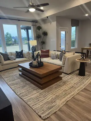 A cozy living room with plush sofas, layered wood coffee table, textured rug, and ample natural light through large windows.