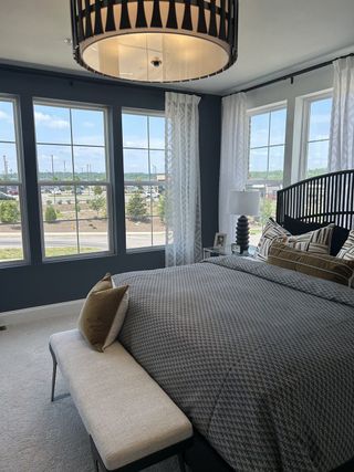 A cozy bedroom featuring large windows, elegant bedding, a stylish bench, and a chic pendant light.