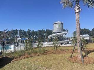 A community pool with a water slide and lush landscaping in Pine Hills at Cane Bay by D.R. Horton (Summerville, SC).