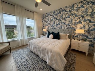 A cozy bedroom featuring a blue-patterned accent wall, elegant white bedding, and ample natural light from large windows.