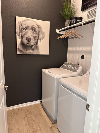A cozy laundry room featuring modern appliances, wood flooring, and charming dog artwork on dark walls.