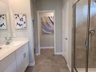 Model Home A modern bathroom with elegant tile flooring, artwork, a sleek shower, and a dual-sink vanity.