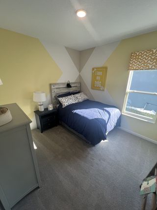 Model Home A cozy bedroom with unique geometric walls, a wooden headboard, and ample natural light creating a warm, inviting space.