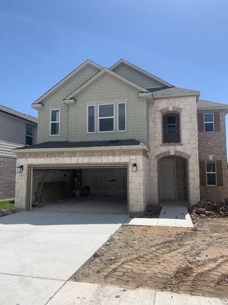 Street view A charming two-story home with a stone and brick exterior, two-car garage, and modern design in Scenic Pass by KB Home (Austin, TX).