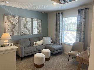 A contemporary living space with a grey sectional sofa, abstract art, textured ottomans, and a window with patterned drapes, creating a stylish retreat.
