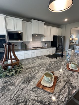 Model Home A modern kitchen with white cabinetry, granite countertops, and stainless steel appliances creates an inviting cooking space.