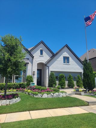 Street view A charming white brick home with manicured landscaping in Sandbrock Ranch by David Weekley Homes (Aubrey, TX).