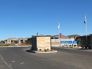 Entrance to The Enclave on Olive by Meritage Homes in Waddell, AZ, showcasing a sleek brick guardhouse and spacious roadways.