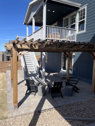 A beautiful covered deck with white railings and a wooden pergola shading a cozy paver patio.