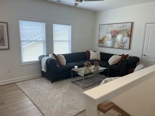 A cozy living room with a dark sectional, abstract artwork, and a glass coffee table on a light rug.