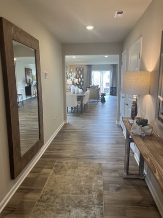 Model Home A welcoming hallway leading to a bright living area with wood flooring, elegant decor, and large windows.