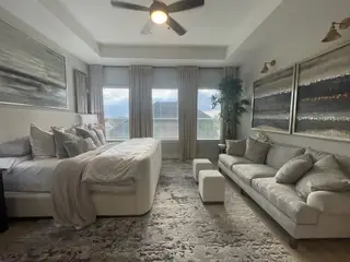 A luxurious bedroom featuring a plush bed, elegant sofa, and abstract art, illuminated by natural light.