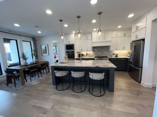 A modern kitchen featuring a marble island, sleek cabinetry, and elegant pendant lighting, opens to a spacious dining area.