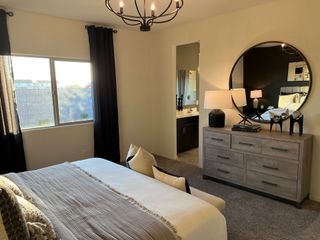 A cozy bedroom featuring a stylish chandelier, plush bedding, large mirror, and elegant decor with natural light streaming in.