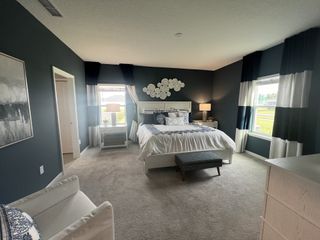 A cozy bedroom with dark walls, elegant bedding, and large windows providing natural light.