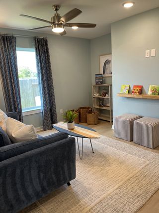 Model Home A cozy living area with a blue sofa, modern ceiling fan, and stylish accents, perfect for relaxation and play.