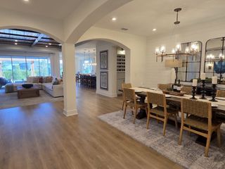 An elegant open-plan living and dining area with wood floors, arched doorways, and chic lighting.