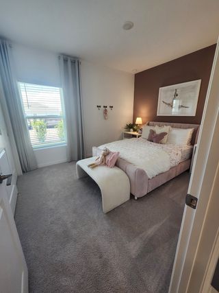 Model Home A cozy bedroom with soft carpeting, a plush bed, accent wall, and elegant drapes. Perfectly inviting and stylish.
