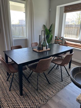 A modern dining area featuring a sleek black table, stylish chairs, and a cozy window seat with natural light.